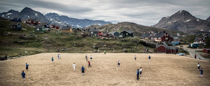 a group of people playing soccer on top of a sandy field in front of mountains