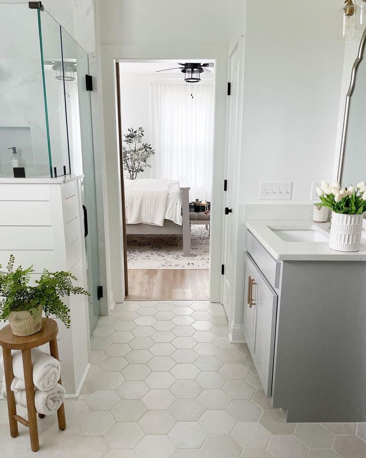 a white bathroom with hexagonal tile flooring and an open door leading to the bedroom