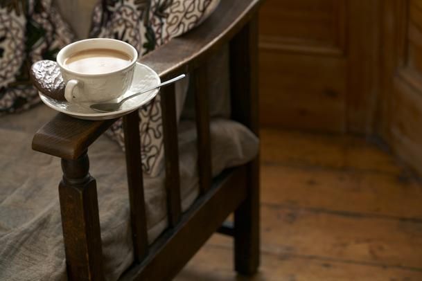 a cup of coffee sitting on top of a wooden bench next to a pillow and blanket