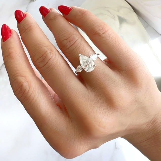 a woman's hand with red nail polish holding a diamond ring