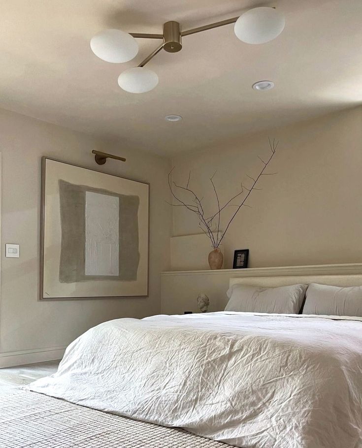 a bed with white sheets and pillows in a bedroom next to a painting on the wall