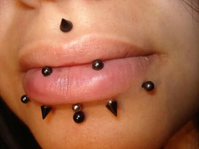 a woman with black spikes on her lip and nose piercings attached to her tongue