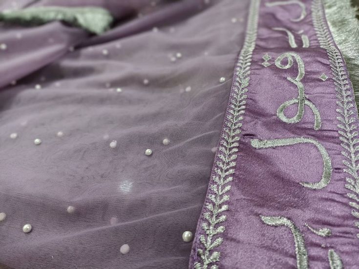 a purple and green bed spread with silver beads on the edges, along with an embroidered monogram