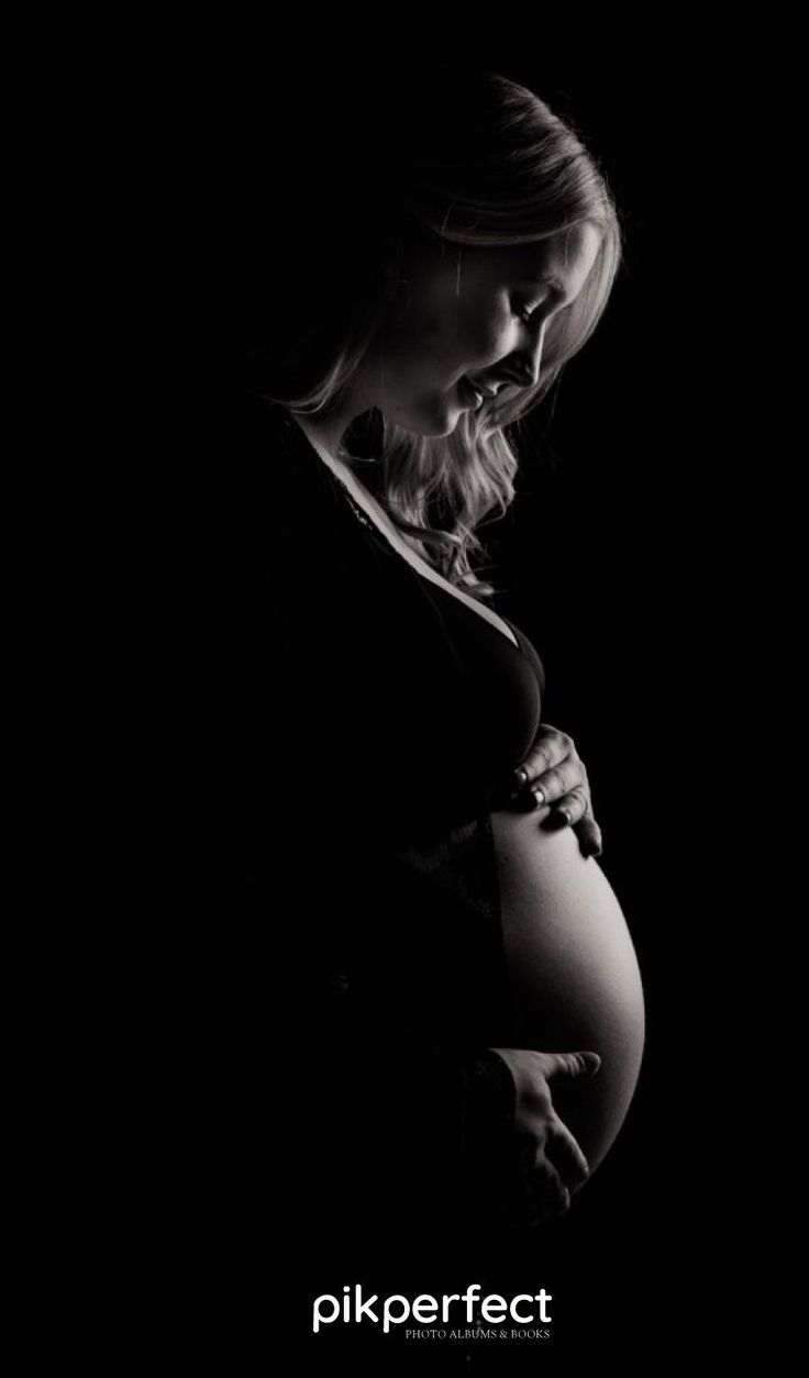 a pregnant woman in the dark with her hands on her belly