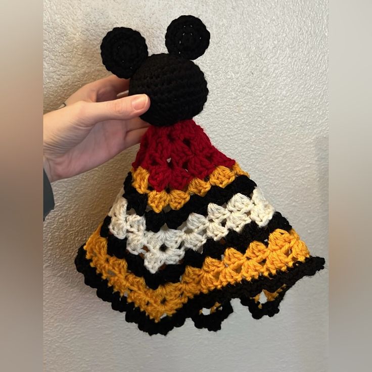 a hand holding up a crocheted mickey mouse hat on a white wall background