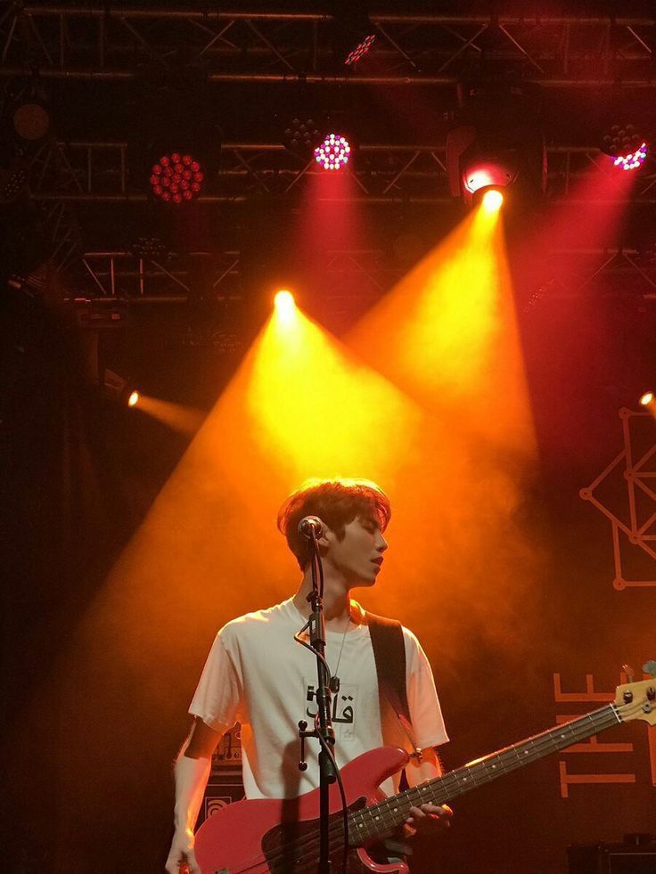 a young man standing in front of a microphone and bass guitar on stage at a concert