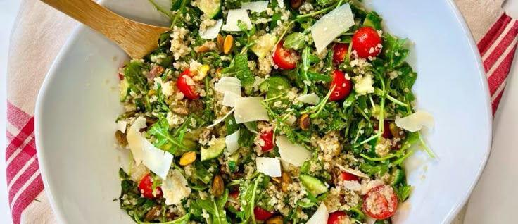 a white bowl filled with salad on top of a red and white table cloth next to a wooden spoon