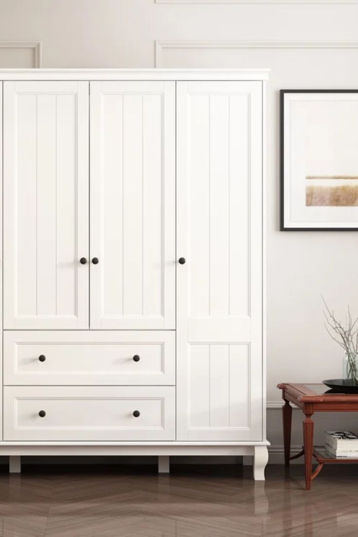 a white armoire in a living room next to a coffee table and framed pictures