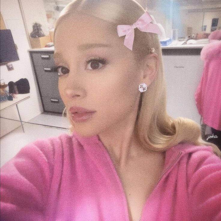 a woman with blonde hair wearing a pink robe and bow in her hair is taking a selfie