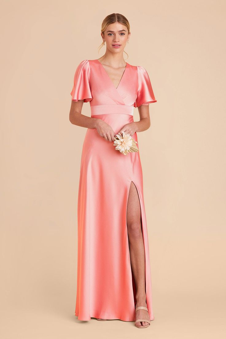 a woman in a long pink dress with a slited skirt and short sleeves, holding a flower