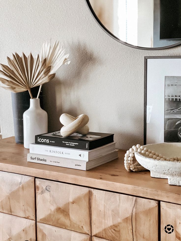 a wooden dresser topped with books and vases next to a framed photograph on top of it