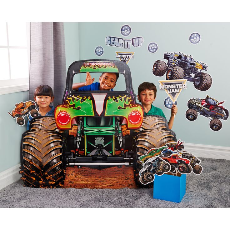 two boys are sitting in the back of a monster truck with their arms up and hands out