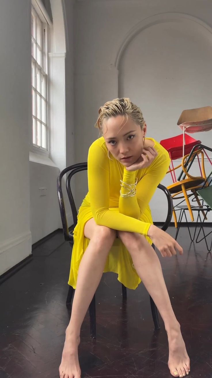 a woman sitting on top of a chair with her legs crossed and wearing a yellow dress