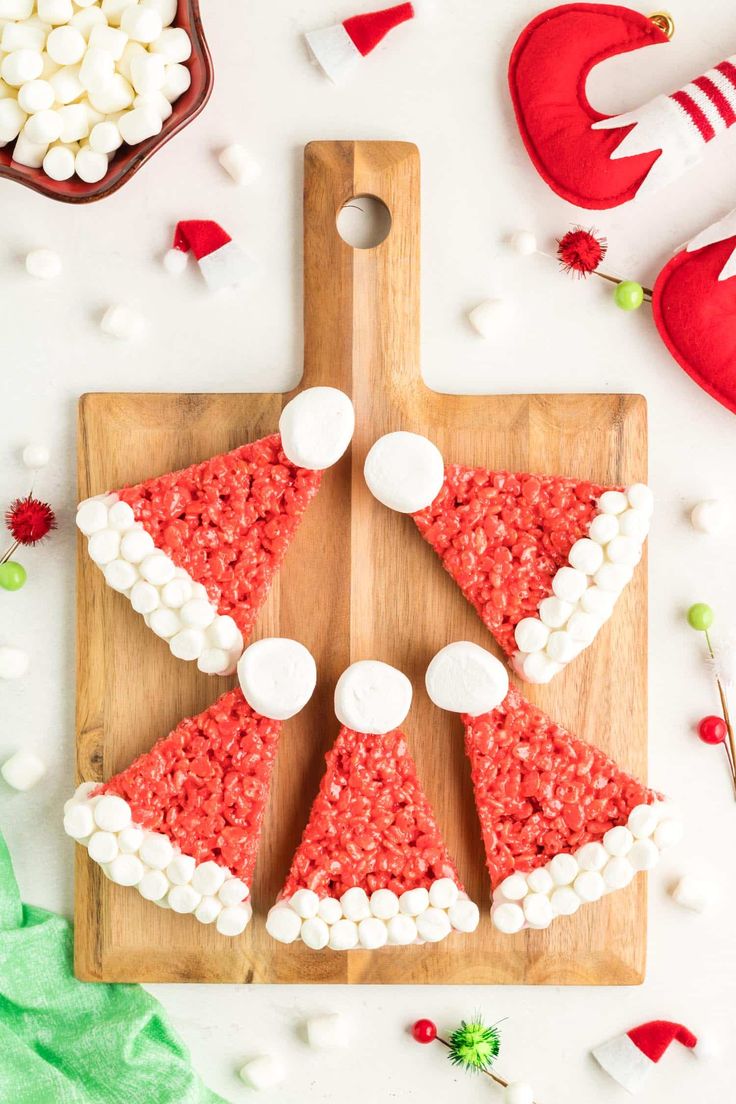 a wooden cutting board topped with red rice krispy kreme christmas tree treats