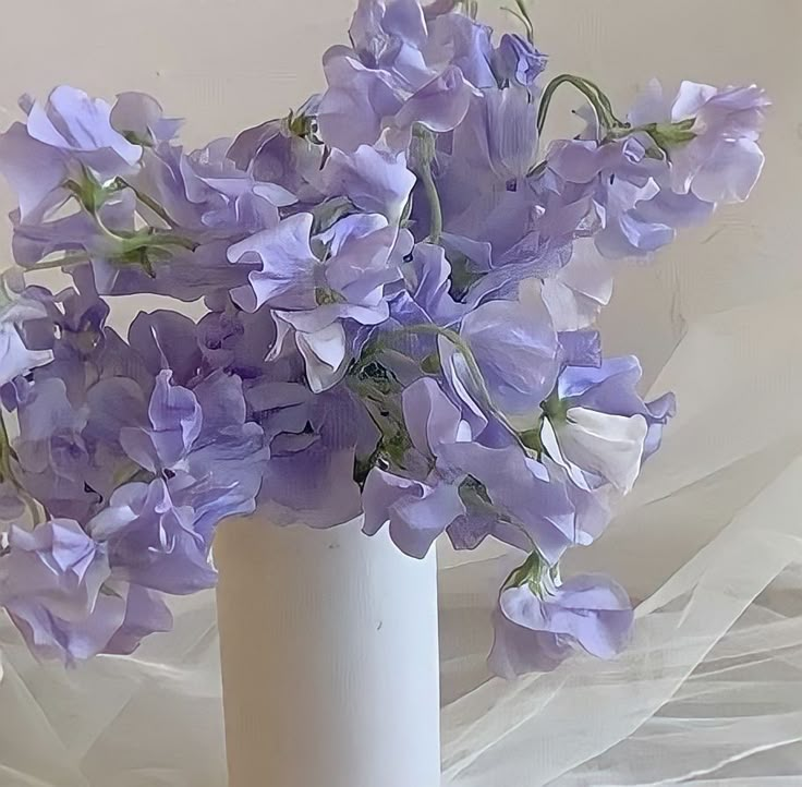 a white vase filled with purple flowers on top of a table