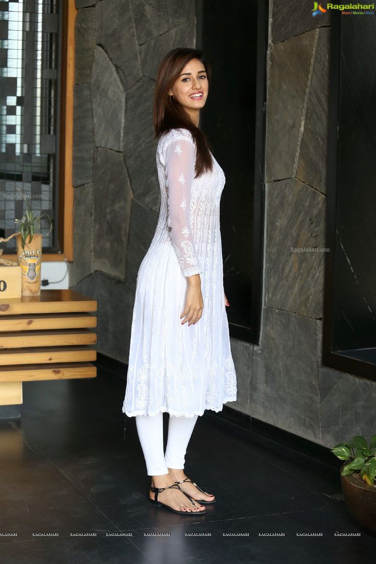 a woman standing in front of a stone wall with her hands on her hips and smiling at the camera