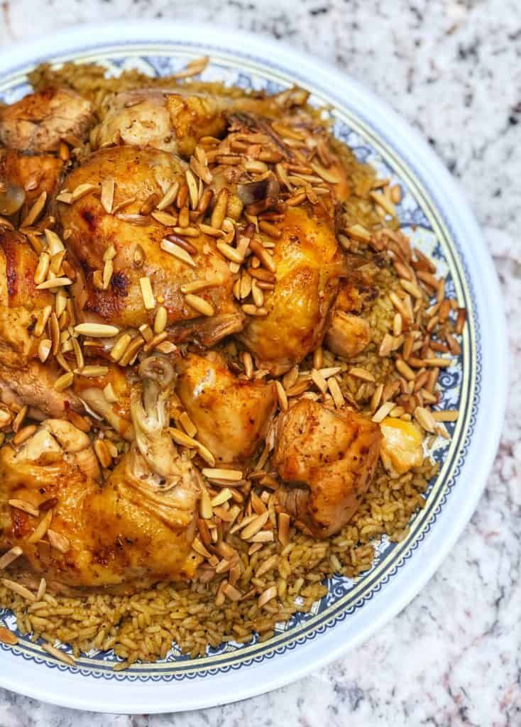 a plate full of chicken and rice on top of a marble table with silverware