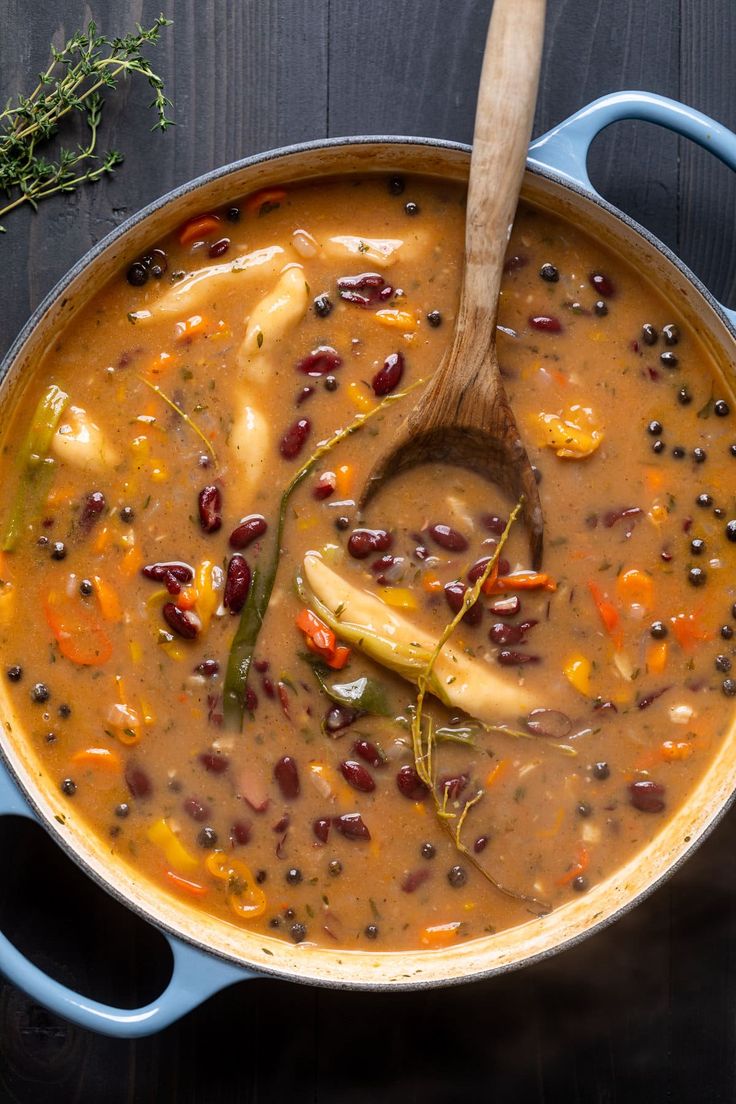 a pot filled with beans, carrots and other vegetables next to a wooden spoon