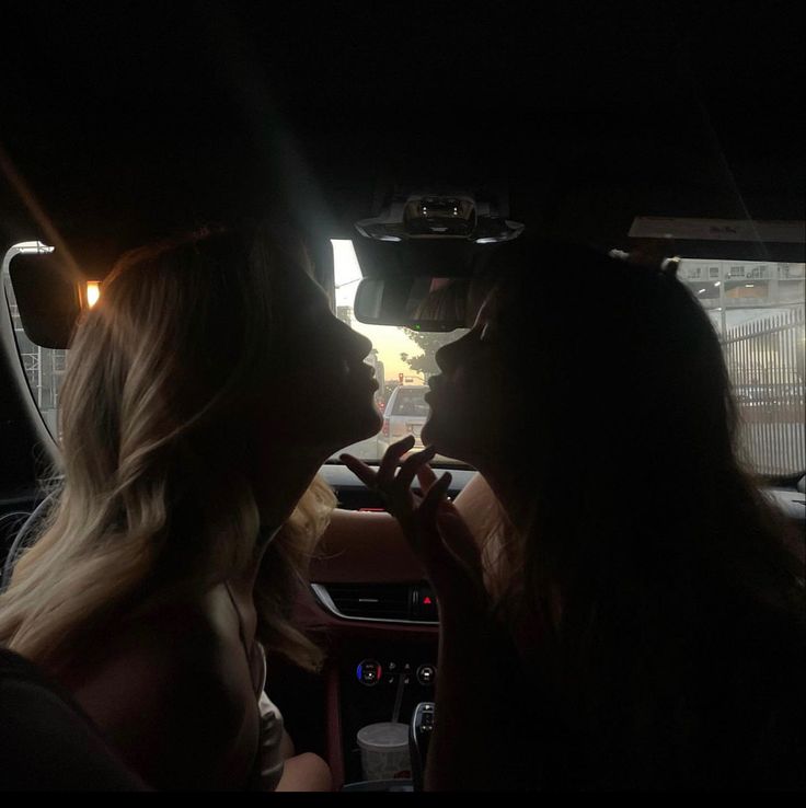 two women sitting in the back seat of a car with their heads turned to look at each other