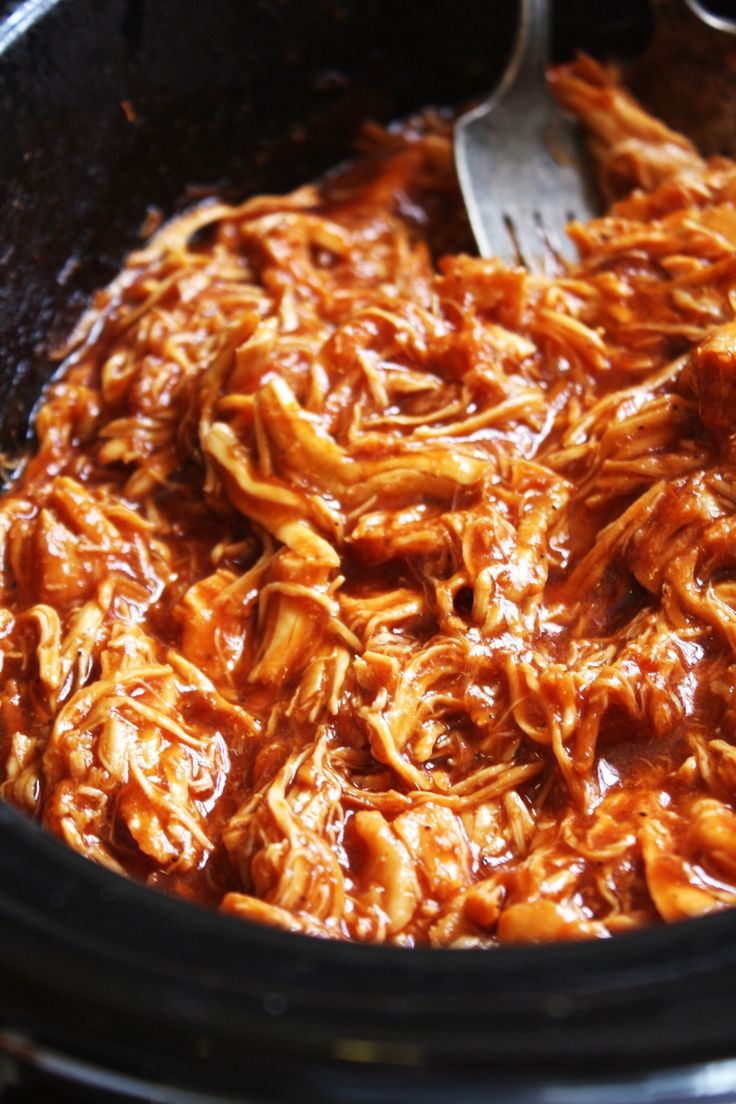 a crock pot filled with shredded meat and a spoon