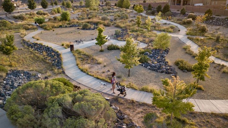 two people walking down a path in the middle of a park with trees and rocks