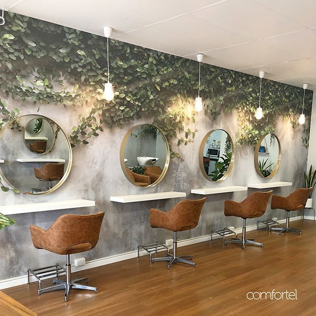 a hair salon with mirrors and chairs in front of plants on the wall behind them