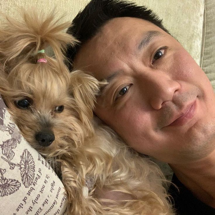 a man laying on top of a couch holding a small dog next to his face