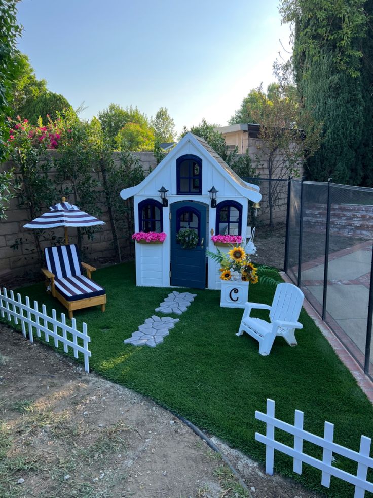 a small white house with lawn chairs and sunflowers on the grass in front of it