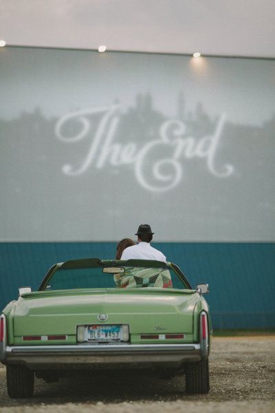 two people sitting in the back of a green convertible car near a movie screen with the word, the end written on it