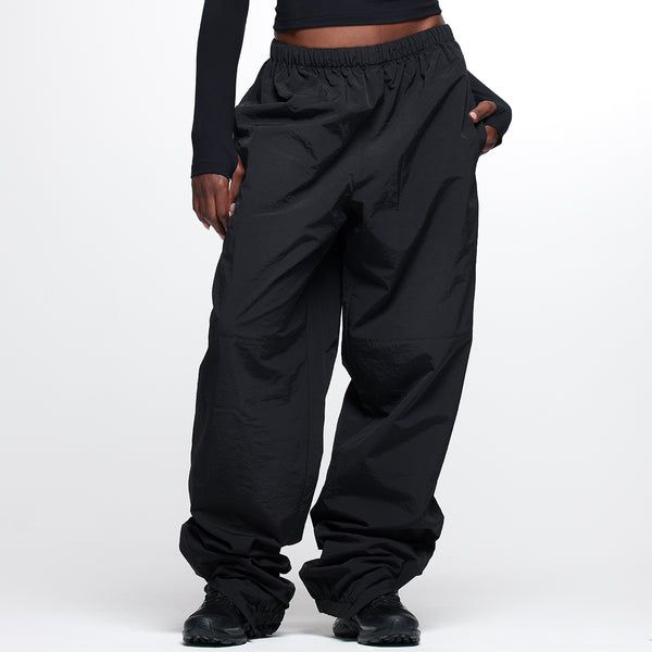 Track Pant - Black Functional Parachute Pants For Outdoor Activities, Functional Winter Parachute Pants With Cargo Pockets, Winter Functional Parachute Pants With Cargo Pockets, Athleisure Nylon Cargo Pants With Functional Drawstring, Nylon Athleisure Cargo Pants With Functional Drawstring, Utility Nylon Parachute Pants With Drawstring, Sporty Nylon Cargo Pants With Functional Drawstring, Nylon Cargo Pants With Functional Drawstring, Nylon Techwear Pants With Functional Drawstring