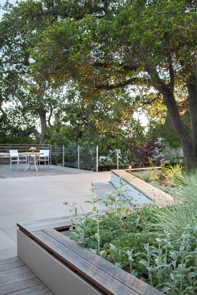 a wooden bench sitting in the middle of a garden next to a tree and table