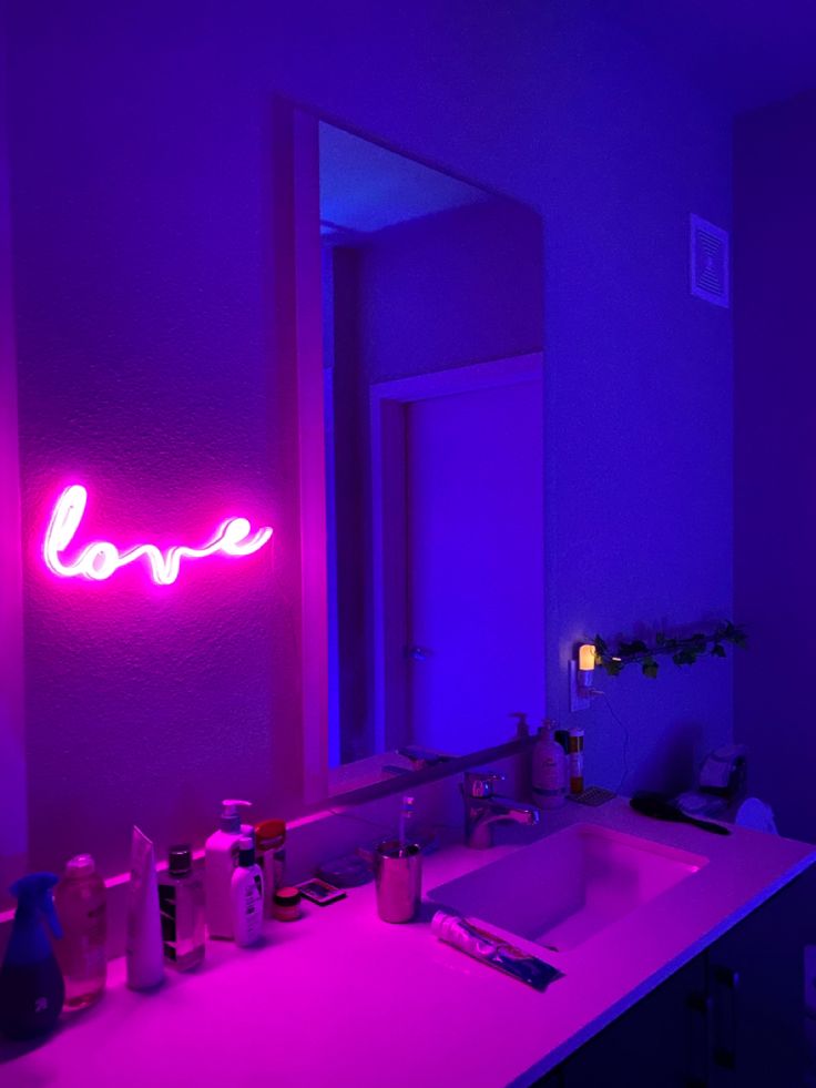 a bathroom with a sink, mirror and neon lights on the wall above it that says love