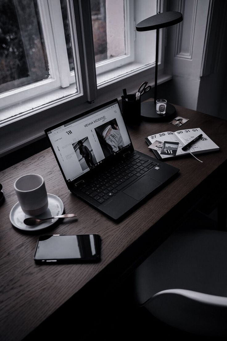 an open laptop computer sitting on top of a wooden desk next to a cup and saucer