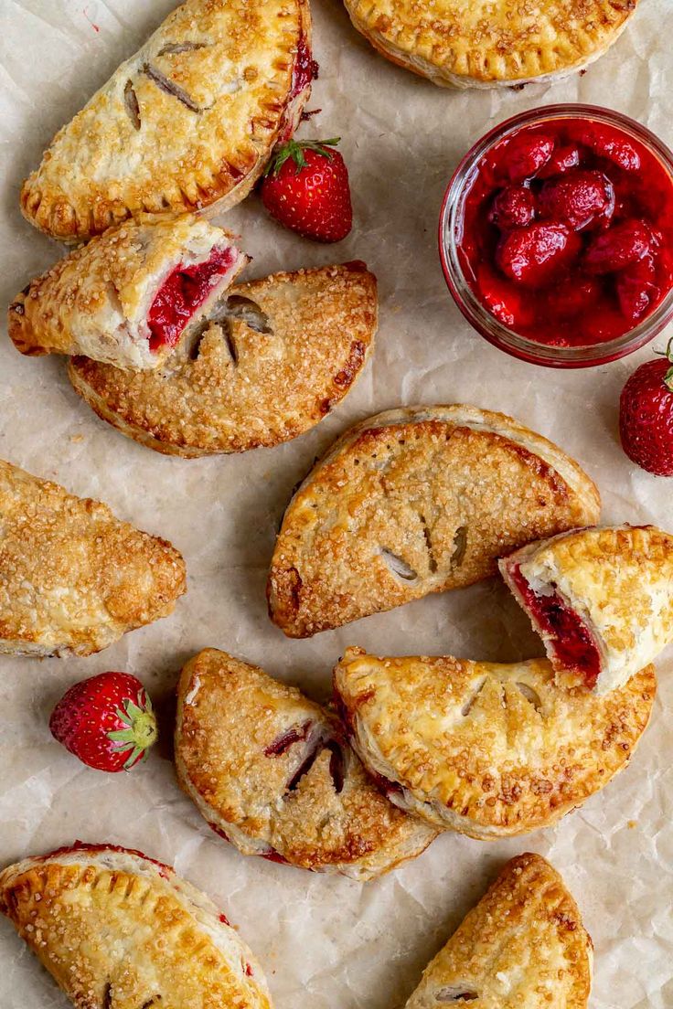 strawberry hand pies with jam and strawberries on parchment paper next to bowl of fruit