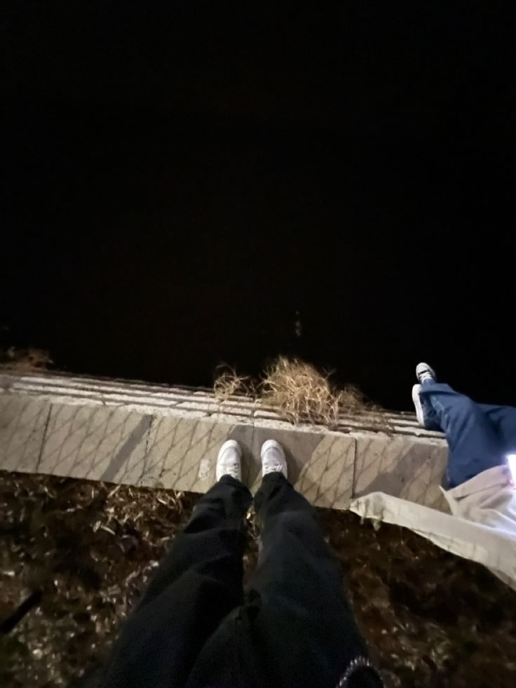 two people standing next to each other in front of a building at night with their feet up