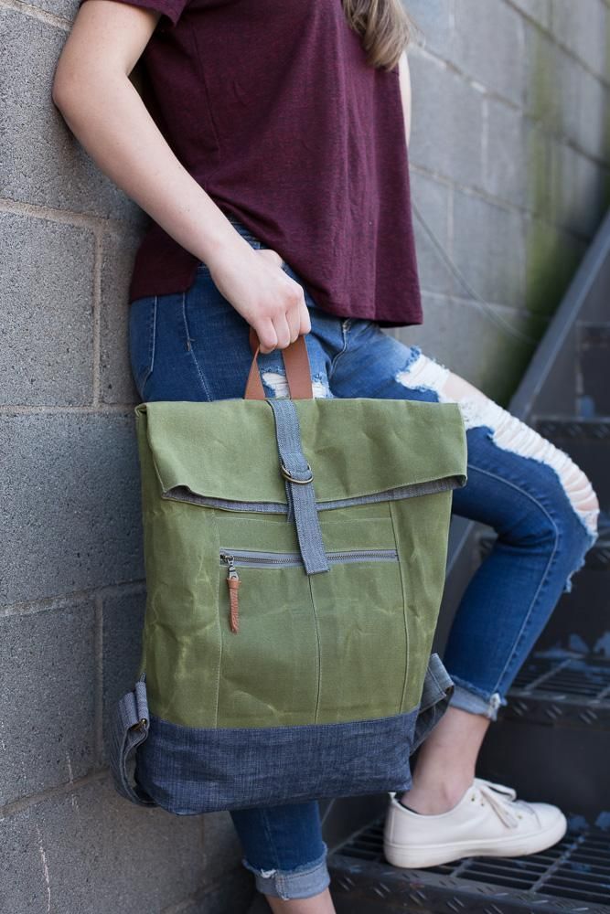 a woman is leaning against a wall holding a green tote bag with zippers