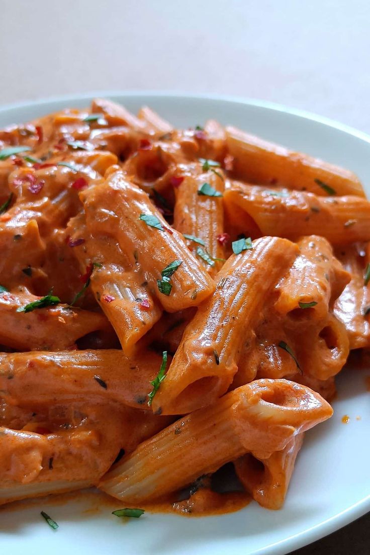 a white plate topped with pasta covered in sauce and garnished with parsley