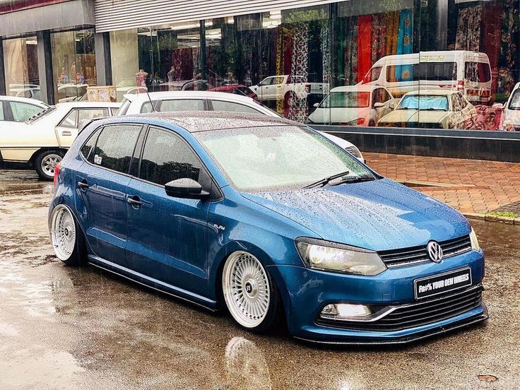 a blue car parked in front of a building on a wet street with other cars behind it