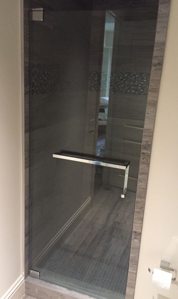 a glass shower door in a bathroom with wood flooring and tile on the walls