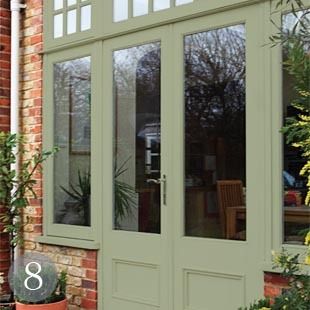 a green double door with glass on the side of a brick building next to potted plants