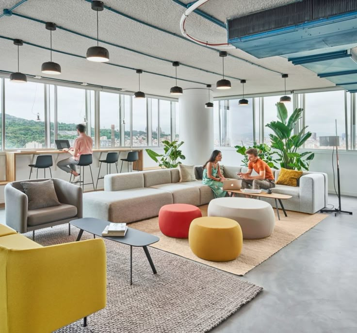 two people sitting on couches in an office with large windows