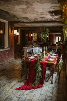 the table is set for christmas dinner with candles and greenery on it, along with other holiday decorations