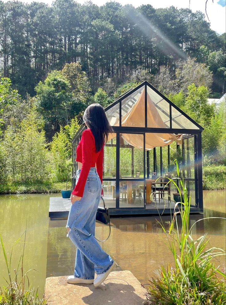 a woman standing on top of a rock in front of a small house next to a lake