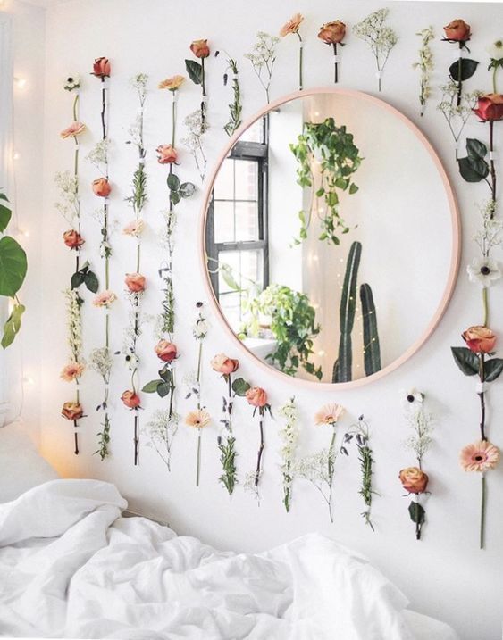 there is a mirror with flowers on the wall and plants hanging from it's sides