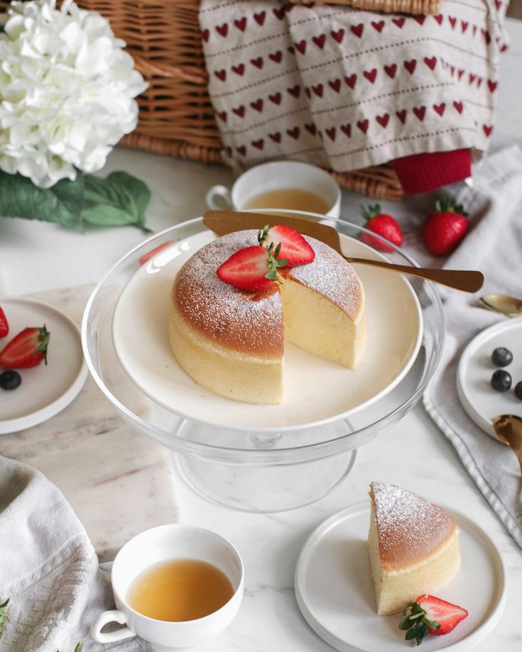 a cake with strawberries on top is sitting on a plate next to cups and saucers