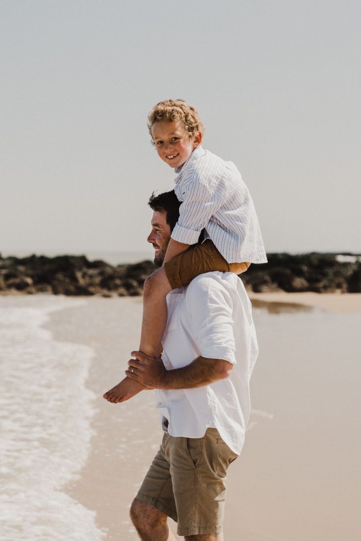 a man carrying a young boy on his back at the beach