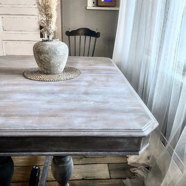 a white vase sitting on top of a wooden table next to a black and white chair