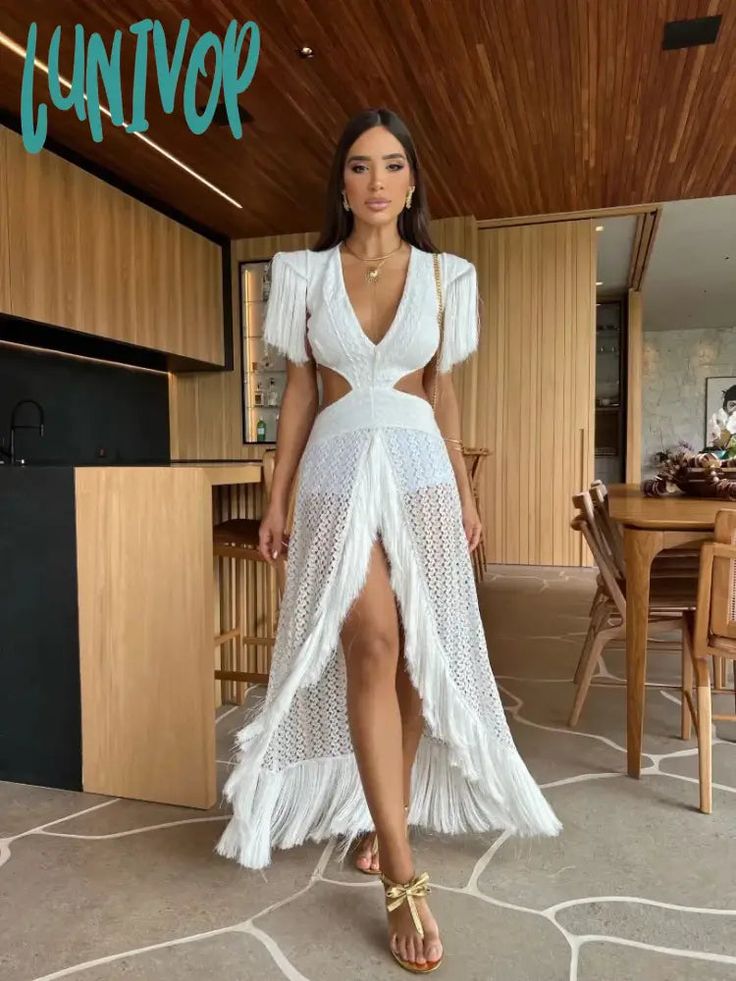 a woman wearing a white dress and sandals standing in front of a table with chairs