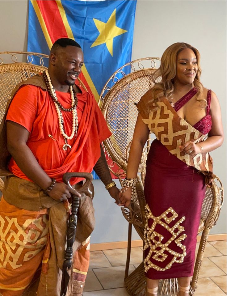 a man and woman dressed in african attire standing next to each other on wicker chairs