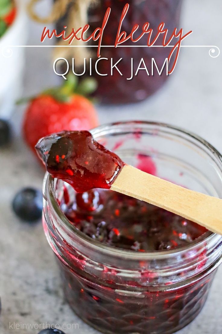 a wooden spoon with jam in it on top of a table next to blueberries and strawberries